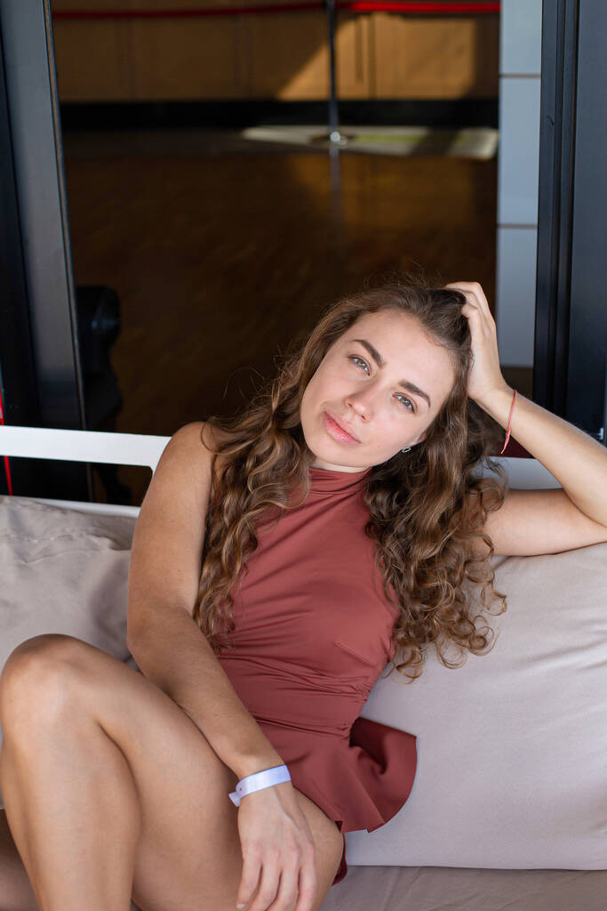 Bílá mladá Evropanka sedící na pohovce s dlouhými kudrnatými vlasy - Fotografie, Obrázek