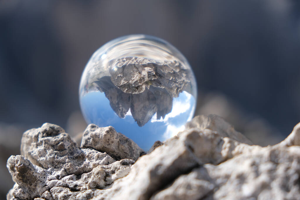Een ondiepe focus shot van een glazen bal met een reflectie van rotsen en lucht - Foto, afbeelding