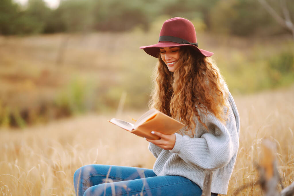 Egy fiatal nő ül egy skótkockán egy őszi parkban egy könyvvel. Őszi piknik a természetben. Egészséges étel. Emberek, életmód, pihenés és nyaralás koncepció. - Fotó, kép