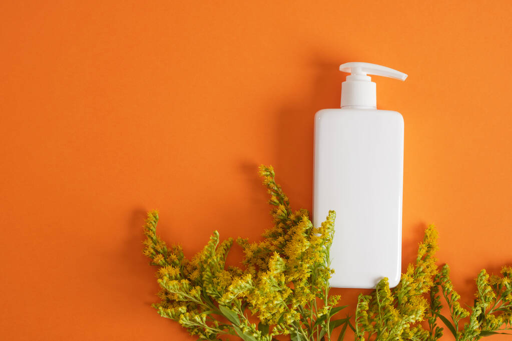 mimosa bloem en drie verschillende blanco witte flessen op een oranje achtergrond, cosmetica mock-up Natuurlijke cosmetische verpakking. mock up schoonheid product concept. - Foto, afbeelding