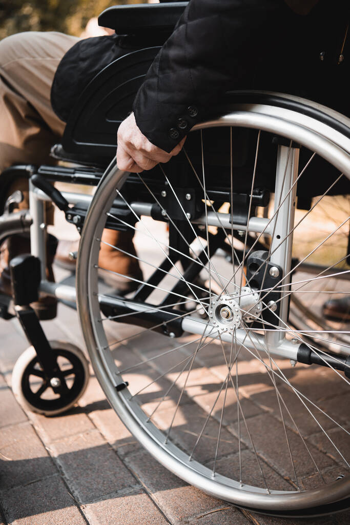 Обрізаний вид на старшого чоловіка, який сидить у інвалідному візку на відкритому повітрі
  - Фото, зображення
