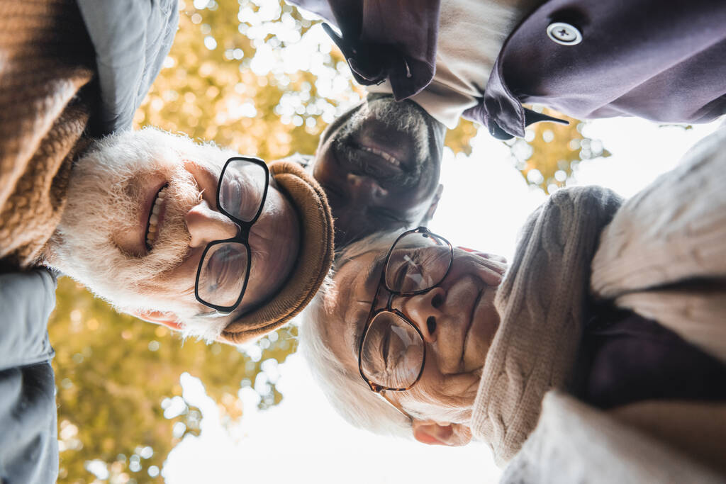 Нижний вид мультикультурных друзей в очках, смотрящих в камеру на улице  - Фото, изображение