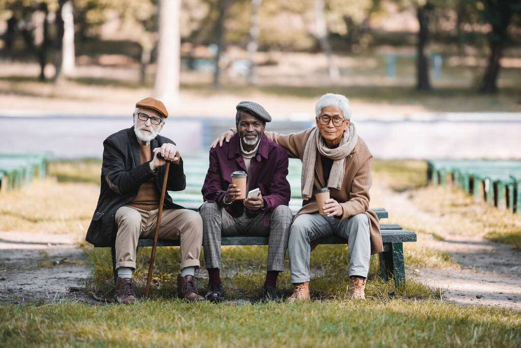 Ältere Freunde mit Coffee to go und Smartphone sitzen auf Parkbank  - Foto, Bild
