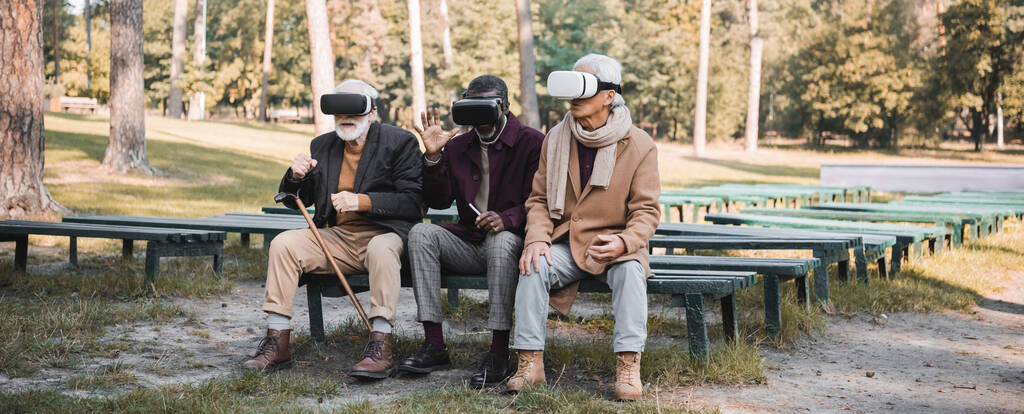 Мультиэтнические старшие мужчины используют наушники vr в осеннем парке, баннер  - Фото, изображение