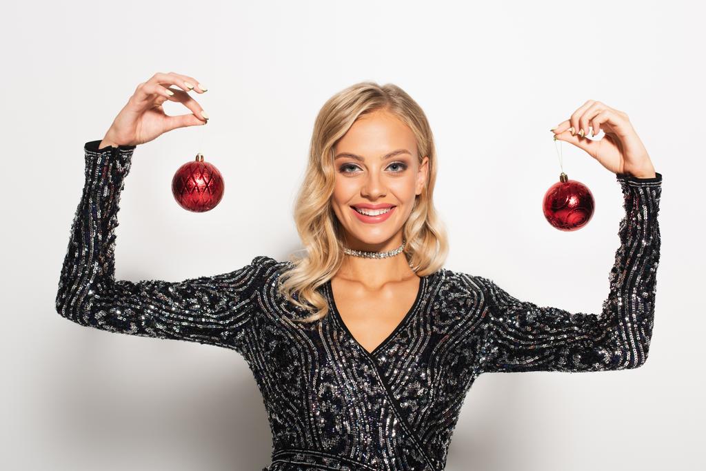 pleased and elegant woman smiling and showing christmas balls on white - Photo, Image