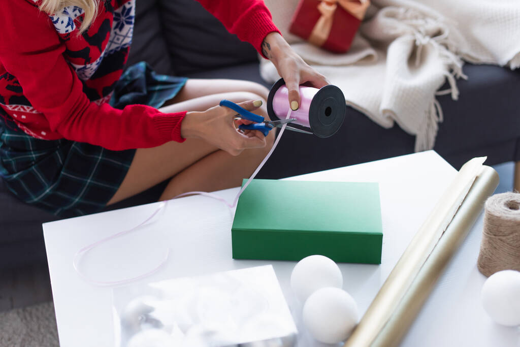 ギフトボックスの近くに装飾的なリボンを切断女性のクロップドビュー,ツイン付きボビン,包装紙とクリスマスボール - 写真・画像