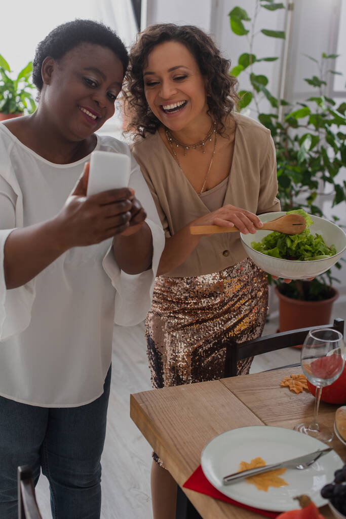 Африканська мама - американка, яка під час обіду показує смартфон на веселій доньці.  - Фото, зображення