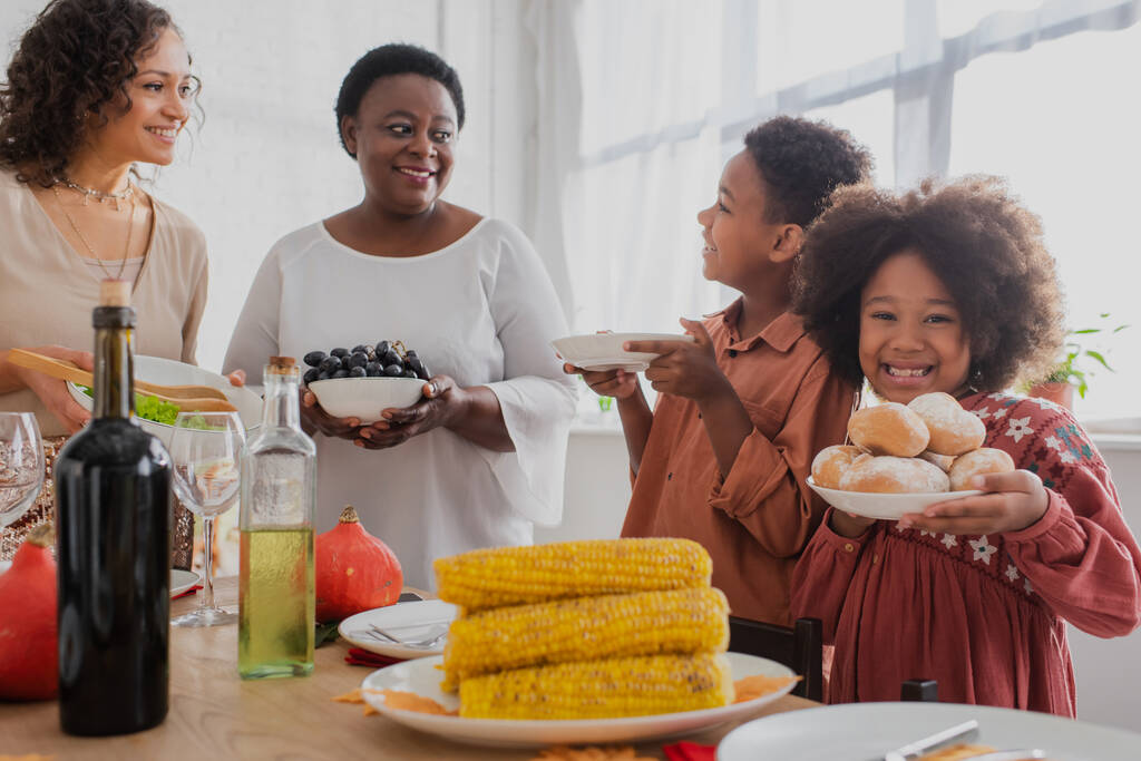 Африканська дівчинка - американка, яка тримає булочки біля своєї сім "ї і готує обід з подякою.  - Фото, зображення