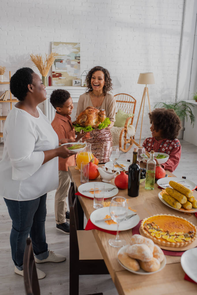 家族の近くで七面鳥を持っているアフリカ系アメリカ人の女性を笑顔と感謝祭ディナー  - 写真・画像