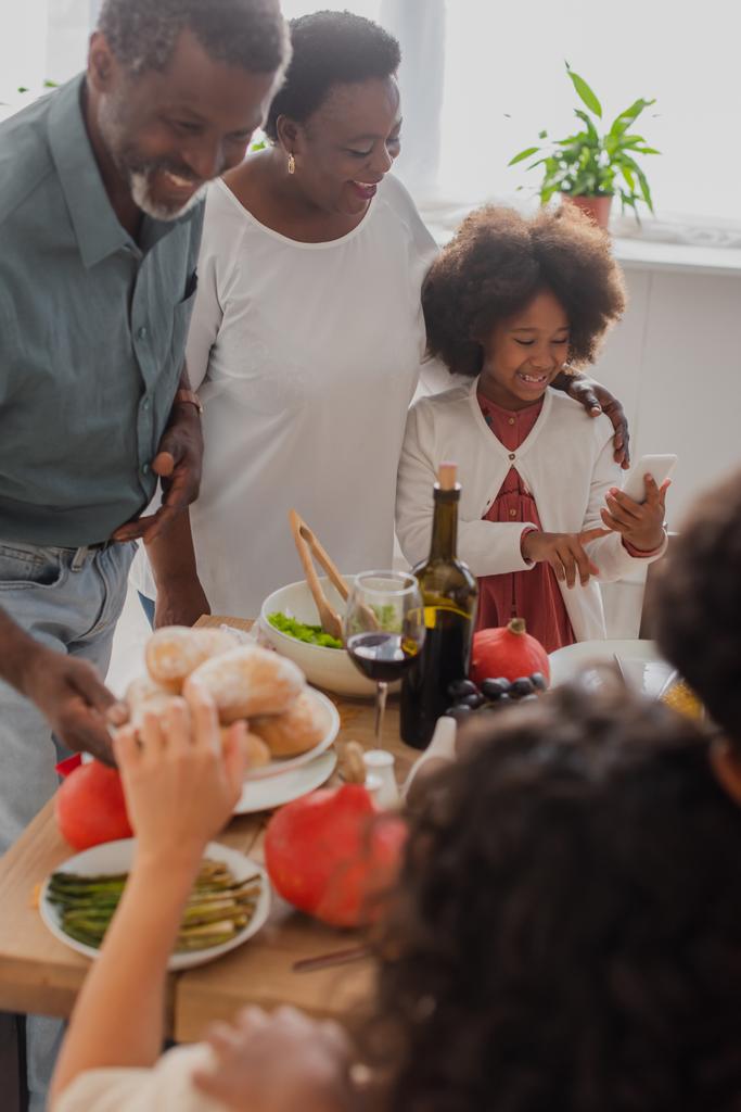 Afrikaans Amerikaans kind met behulp van smartphone in de buurt van grootouders en dankzegging diner  - Foto, afbeelding