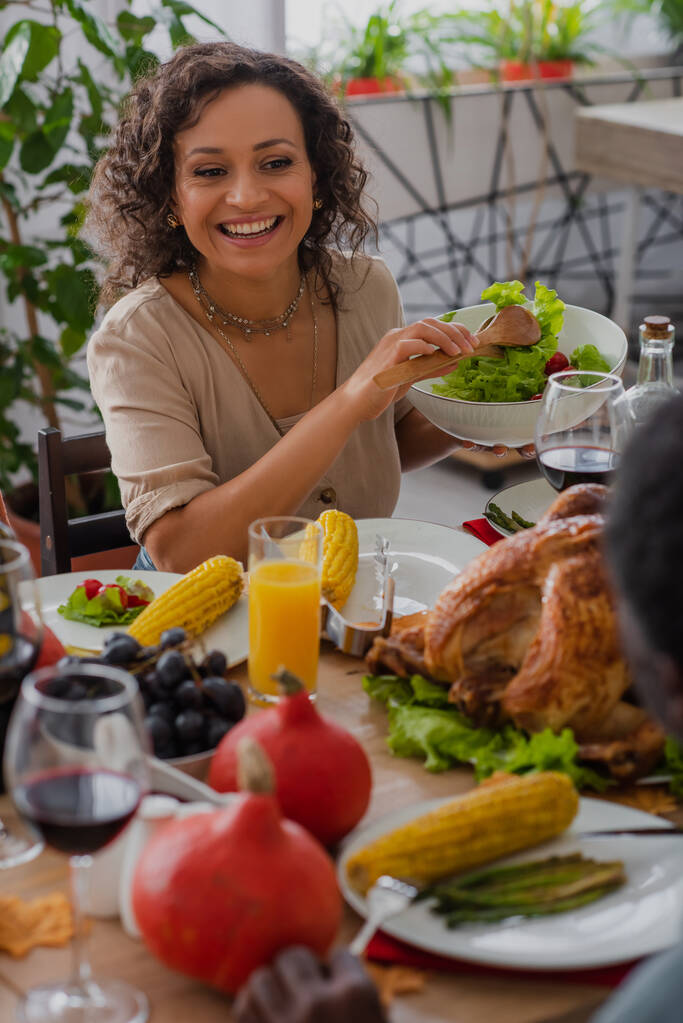 Happy african american mother holding salad near blurred father and traditional thanksgiving dinner  - Photo, Image