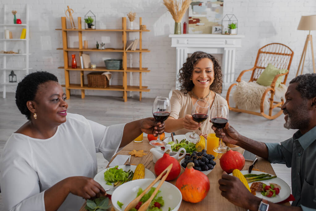 陽気なアフリカ系アメリカ人の両親と大人の娘感謝祭の夕食中にワインをクリック  - 写真・画像