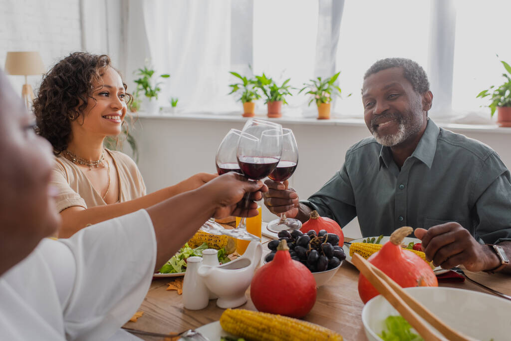 Улыбающаяся африканская американская семья пьет вино во время ужина в честь Дня Благодарения  - Фото, изображение