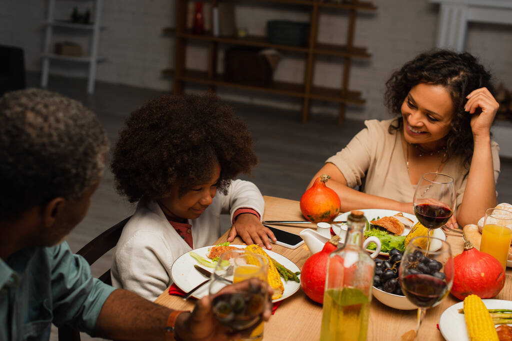 donna afroamericana sorridente durante la cena del Ringraziamento con padre e figlia - Foto, immagini