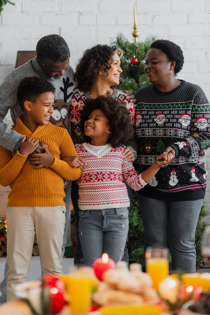 Gülümseyen Afro-Amerikan ailesi evde Noel kutlaması sırasında el ele tutuşuyorlar. - Fotoğraf, Görsel