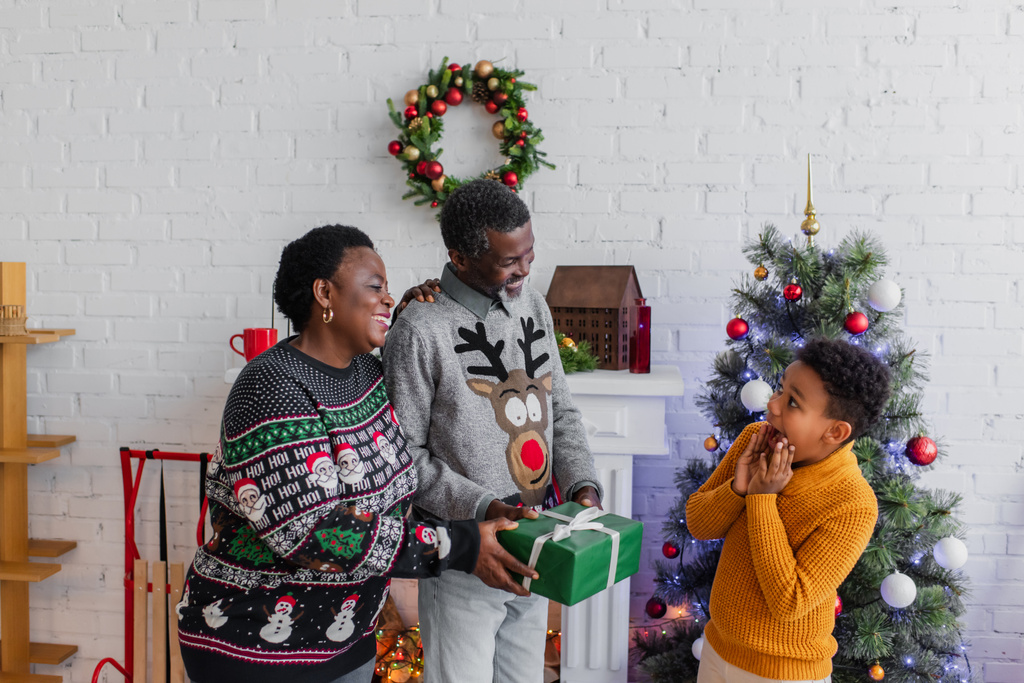 Afrikaans amerikaans paar schenken kerstcadeau aan verbaasd kleinzoon - Foto, afbeelding