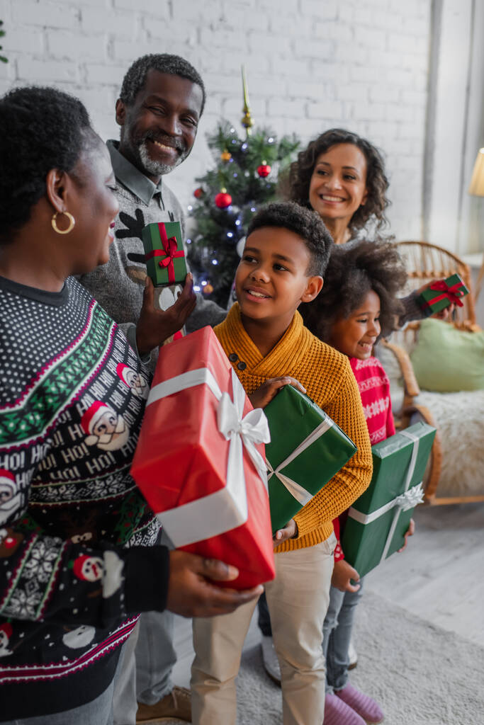 famiglia afro-americana sorridente mentre tiene regali di Natale a casa - Foto, immagini