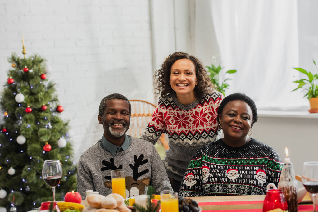 szczęśliwy Afroamerykanka kobieta uśmiecha się blisko dojrzałych rodziców podczas świątecznej kolacji - Zdjęcie, obraz