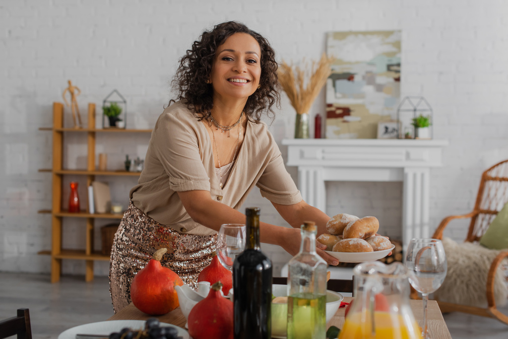 happy african american woman holding homemade buns near table served with thanksgiving dinner - Photo, Image