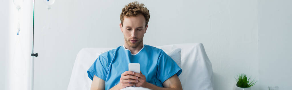 σγουρός ασθενής που χρησιμοποιεί smartphone ενώ ξεκουράζεται στο κρεβάτι του νοσοκομείου, banner - Φωτογραφία, εικόνα