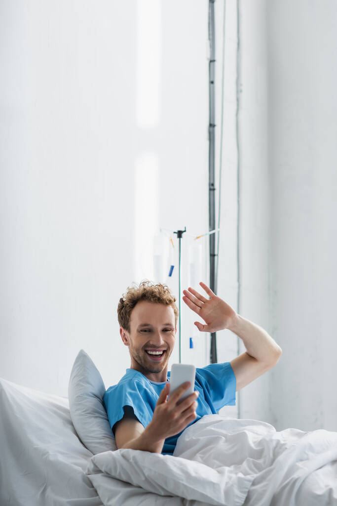 щасливий пацієнт махає рукою, маючи відеодзвінок на смартфон у лікарні
  - Фото, зображення
