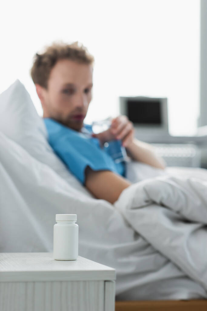 病院のベッドの患者の近くのベッドサイドテーブルで薬を飲む瓶  - 写真・画像
