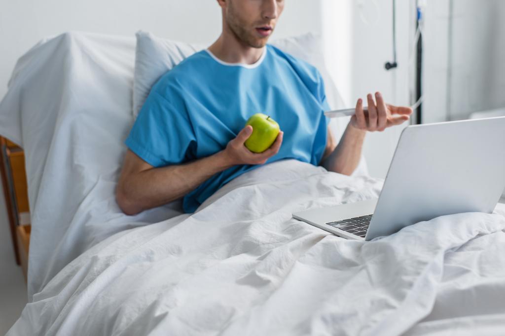 vue recadrée de l'homme malade ayant un appel vidéo tout en tenant pomme à l'hôpital  - Photo, image
