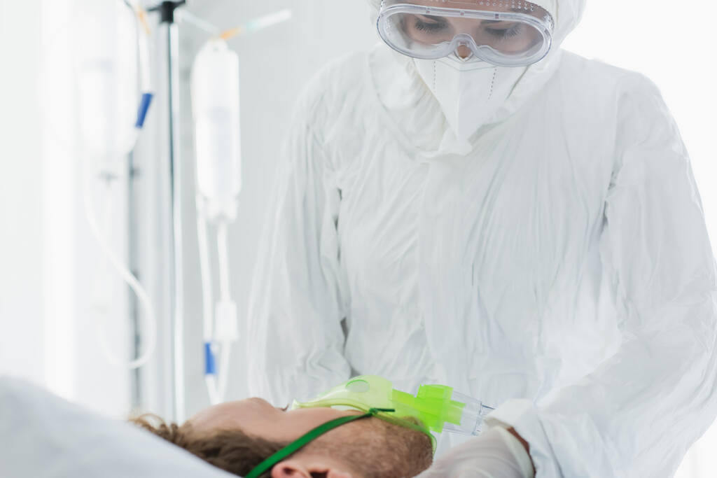 Arzt in persönlicher Schutzausrüstung untersucht Patient in Sauerstoffmaske im Krankenhaus  - Foto, Bild