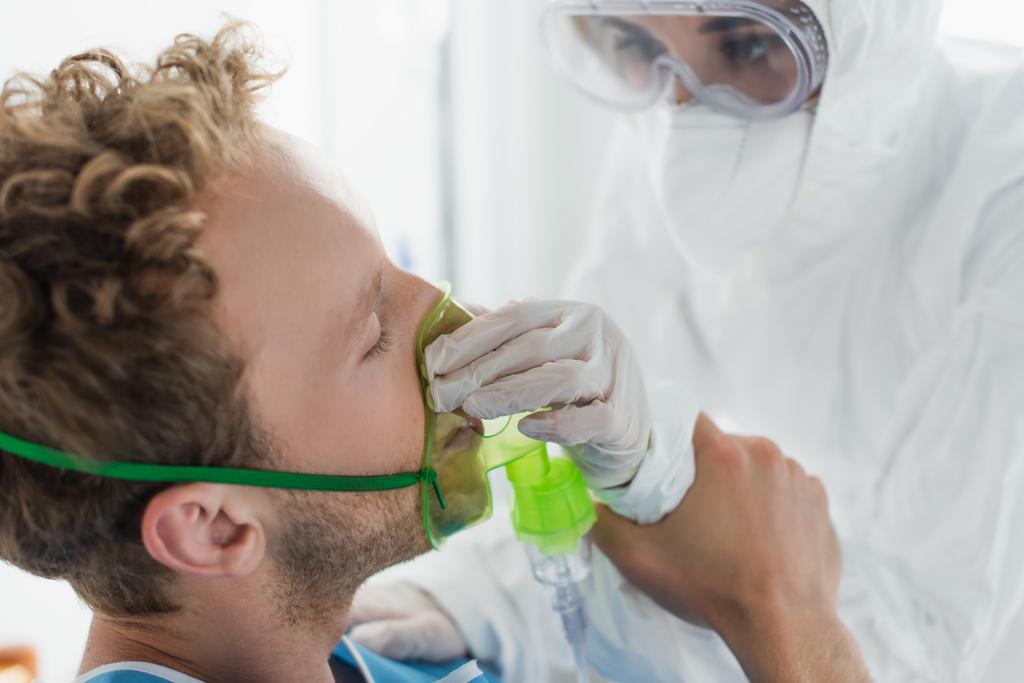 Tehlikeli madde giysisi içindeki doktor hastanedeki hastaya oksijen maskesi takıyor.  - Fotoğraf, Görsel
