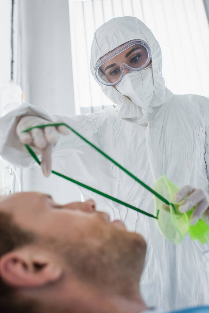 medico in tuta hazmat posa maschera di ossigeno sul paziente offuscato in ospedale  - Foto, immagini