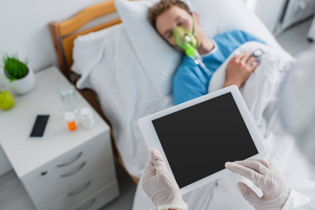высокая угол зрения врача в латексных перчатках проведение цифровой таблетки с пустым экраном рядом с больным пациентом  - Фото, изображение