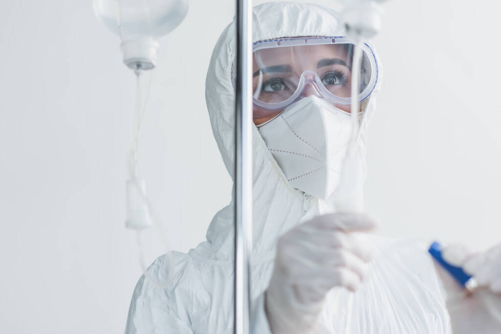 Arzt in persönlicher Schutzausrüstung und Schutzbrille blickt auf Drop Counter - Foto, Bild
