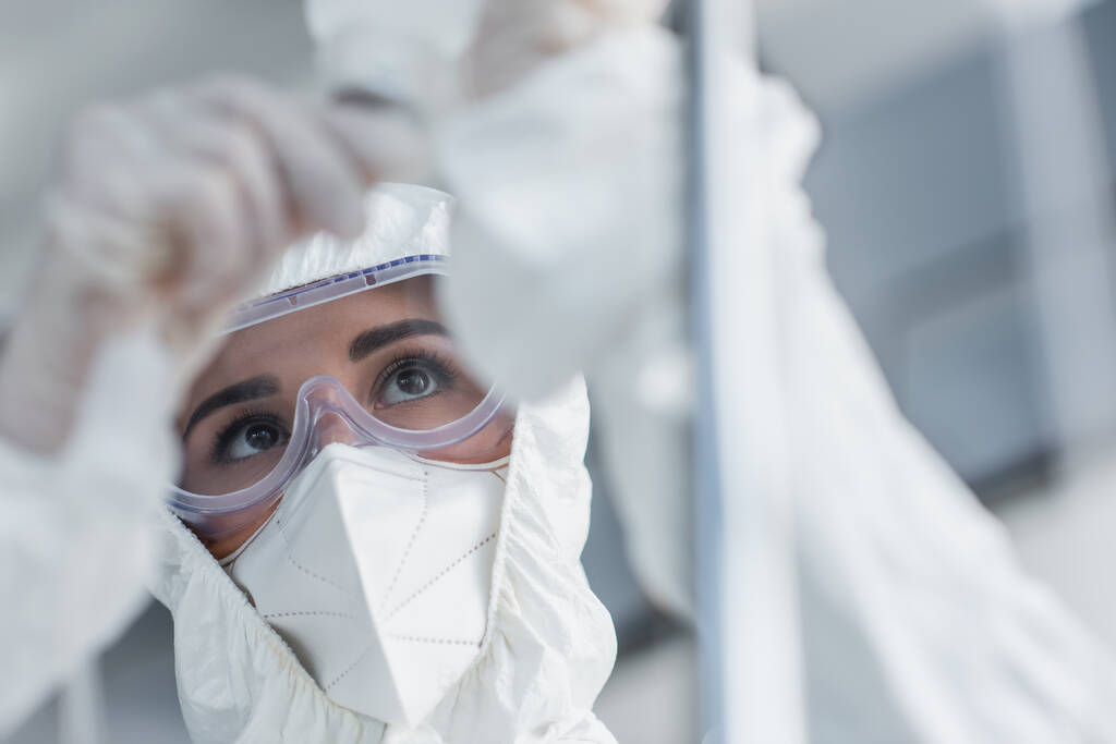 médico en traje de materiales peligrosos, máscara médica y gafas que sostienen el catéter en el mostrador de gotas - Foto, Imagen