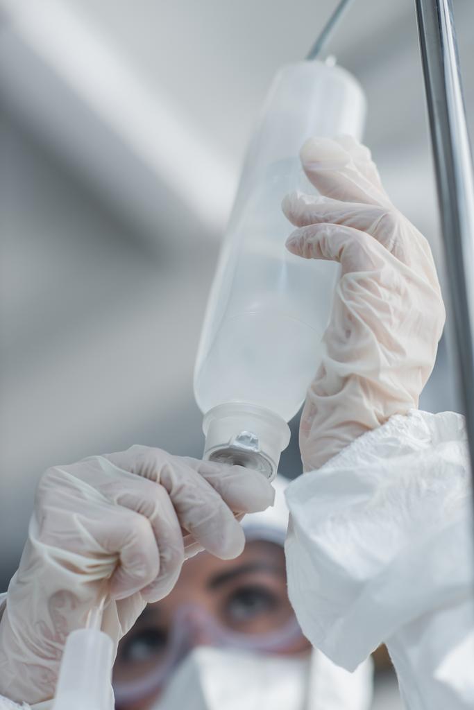 Ausgeschnittene Ansicht eines Arztes in Latexhandschuhen, der einen Katheter auf dem Tropfenzähler hält - Foto, Bild