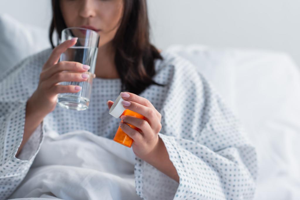 cropped view of sick woman holding bottle with medication while taking pill in hospital  - Photo, Image