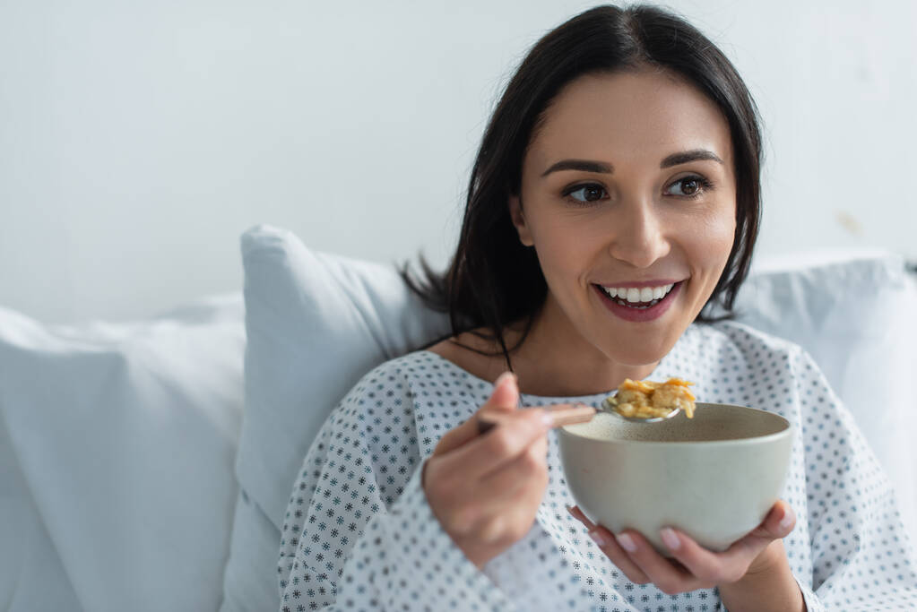 smiling patient holding spoon with corn flakes and bowl in hospital  - Photo, Image
