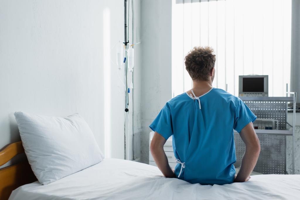visão traseira do homem encaracolado sentado na cama do hospital  - Foto, Imagem