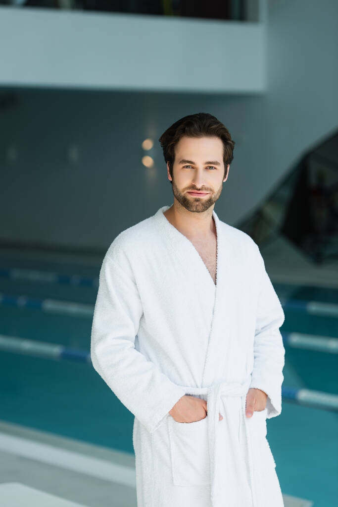 Young man holding hands in pockets of bathrobe in spa center  - Photo, Image