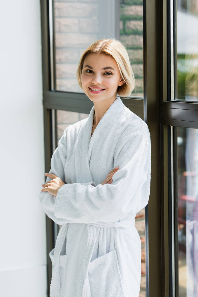Smiling woman in bathrobe standing with crossed arms near window in spa center  - Photo, Image