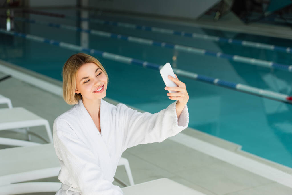 Donna sorridente scattare selfie su smartphone vicino alla piscina nel centro benessere  - Foto, immagini