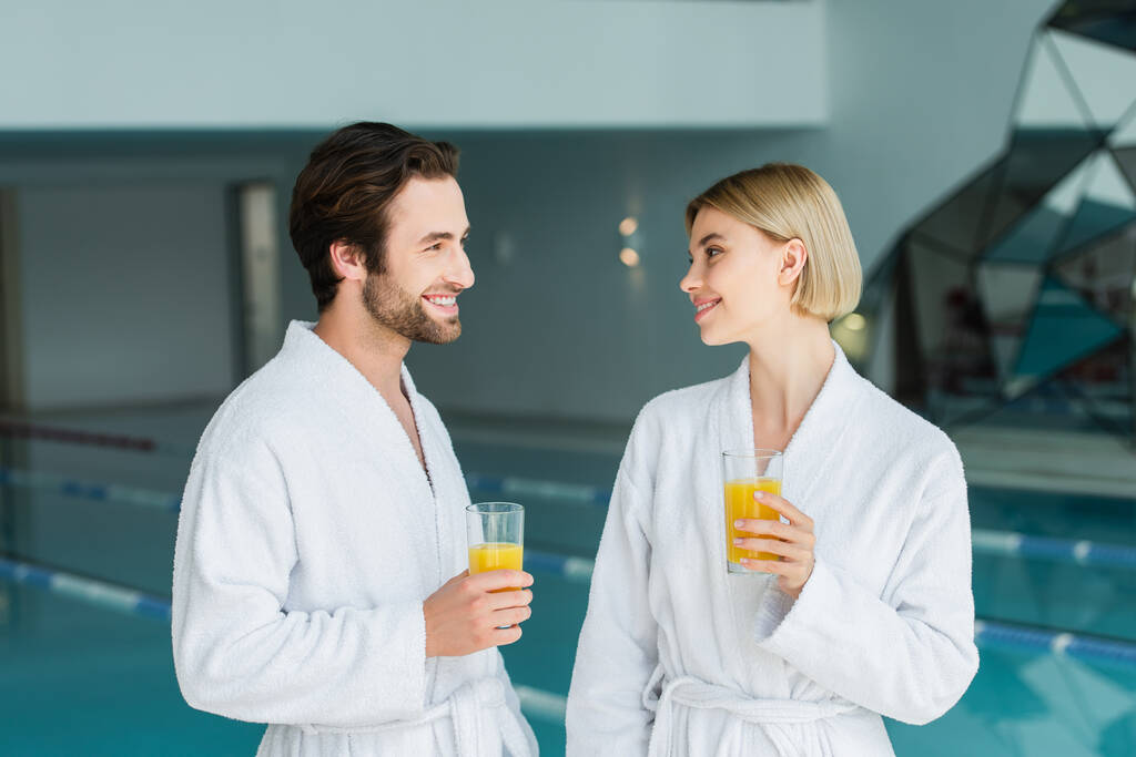 Positives Paar in weißen Bademänteln mit Orangensaft im Kurzentrum  - Foto, Bild