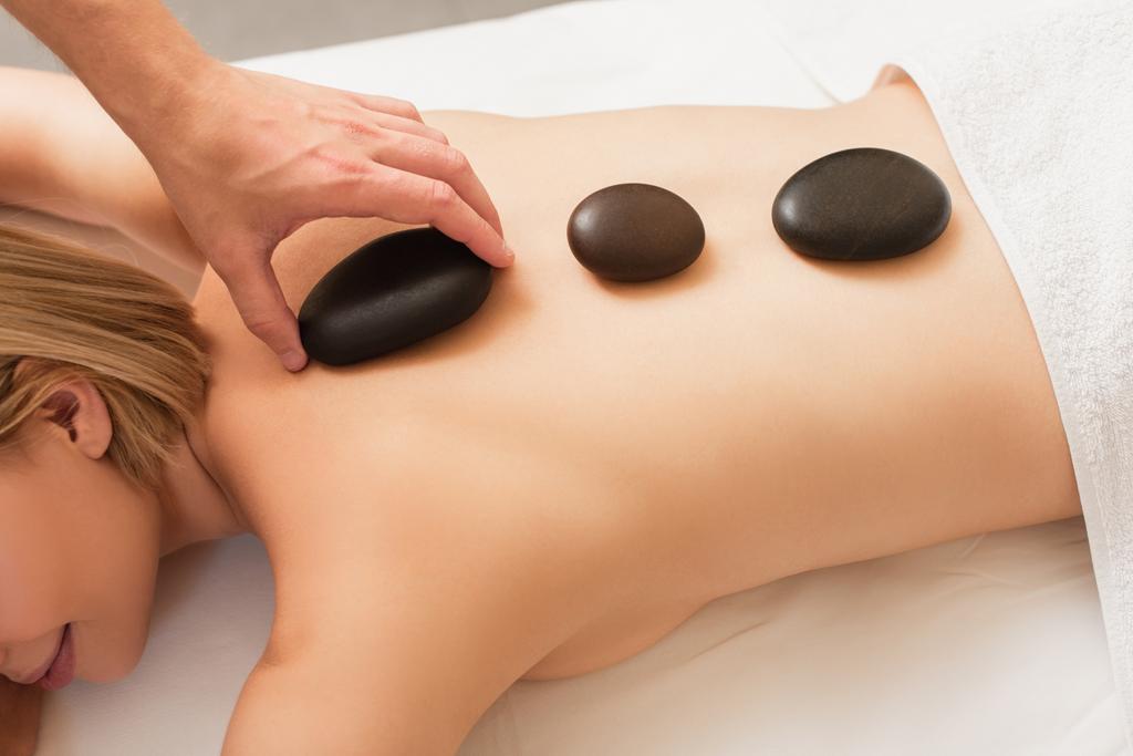 Vue de dessus du masseur mettant la pierre de spa sur le dos de la jeune femme sur la table de massage  - Photo, image