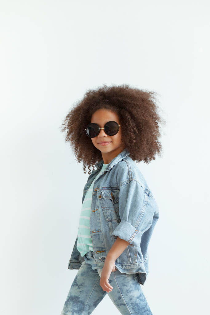 Смішна стильна дівчина з красивим кучерявим волоссям у джинсовому одязі та сонцезахисних окулярах
 - Фото, зображення
