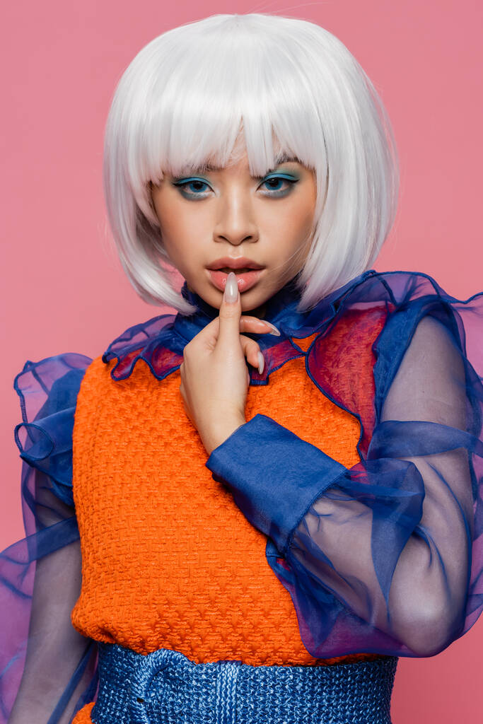 Elegante modelo asiático en estilo pop art tocando los labios aislados en rosa  - Foto, imagen