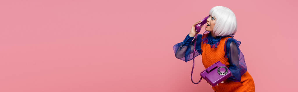 Widok z boku wesoły azjatycki pop art model rozmowy przez telefon odizolowany na różowy, baner  - Zdjęcie, obraz