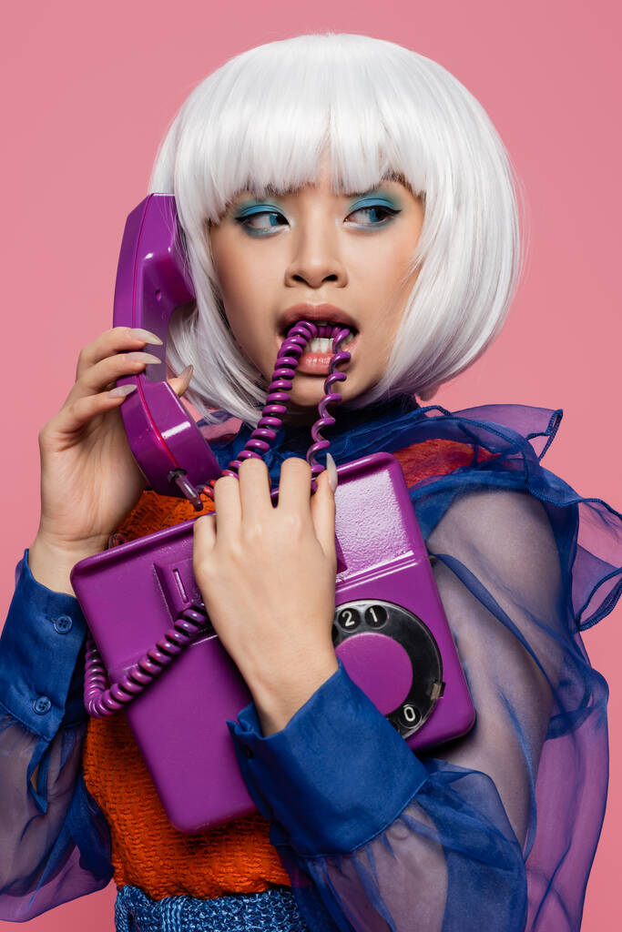 Asiatique pop art modèle mordre câble tout en parlant sur téléphone isolé sur rose  - Photo, image