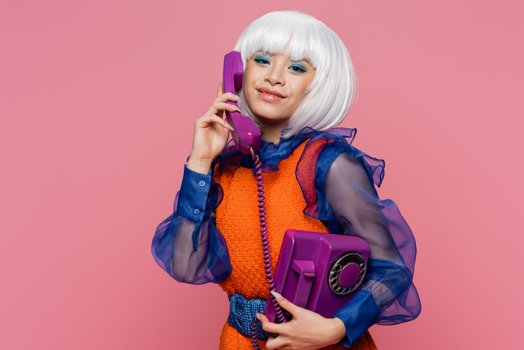 Positivo asiático pop art modelo falando no telefone e olhando para câmera isolada no rosa  - Foto, Imagem