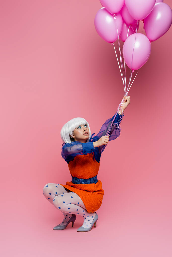 Joven asiático pop arte modelo mirando globos en rosa fondo - Foto, imagen