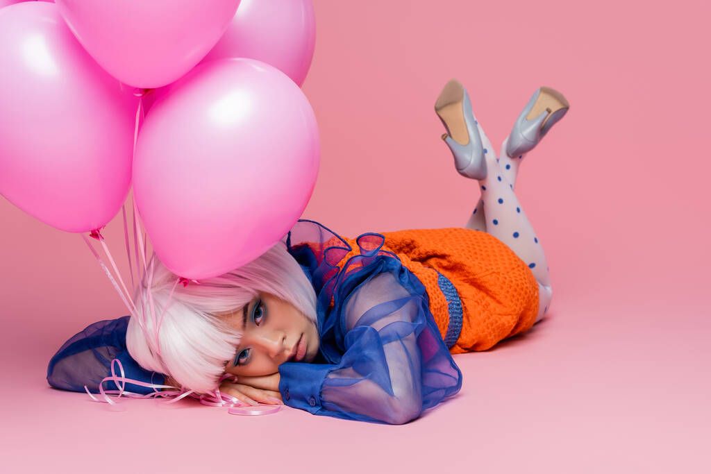 Jolie asiatique pop art modèle couché près de ballons sur fond rose - Photo, image