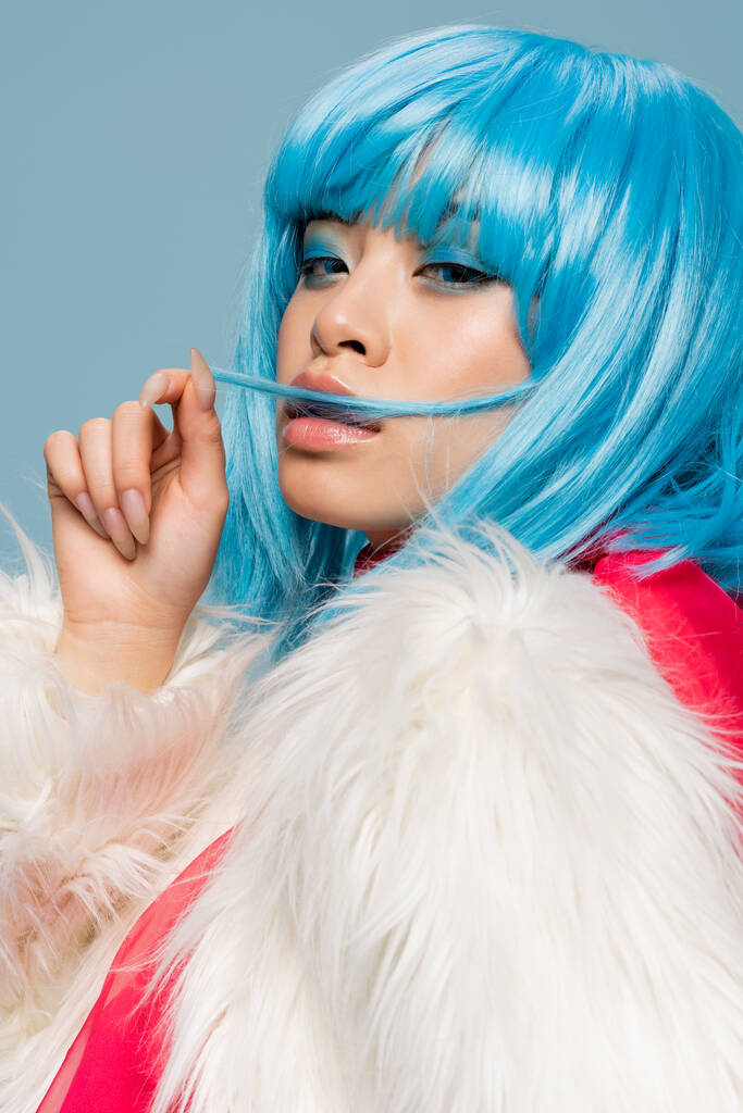 Portrait von stilvollen asiatischen Frau berühren Haare isoliert auf blau  - Foto, Bild